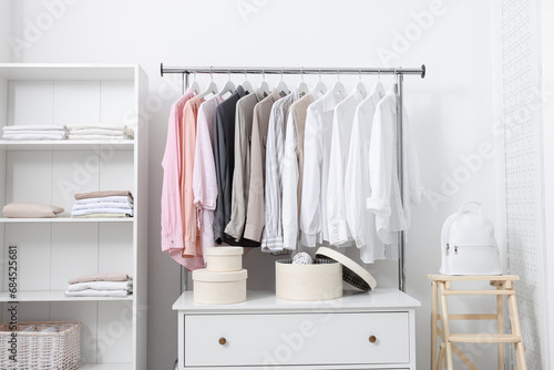 Wardrobe organization. Rack with different stylish clothes, chest of drawers and shelving unit near white wall indoors