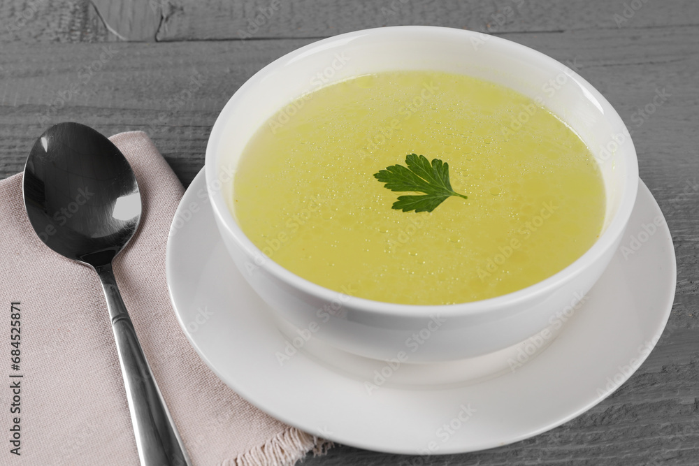 Tasty broth in bowl on grey wooden table, closeup Tasty broth in bowl on grey wooden table, closeup