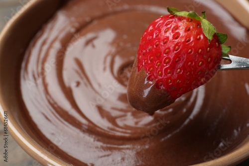Strawberry with melted chocolate on fork above fondue, closeup. Space for text