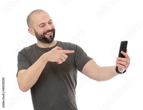 Portrait oh happy man with beard being video call with someone while pointing at the telephone with a happy expression, isolated on white background. Bald forty year old guy posing in studio. photo