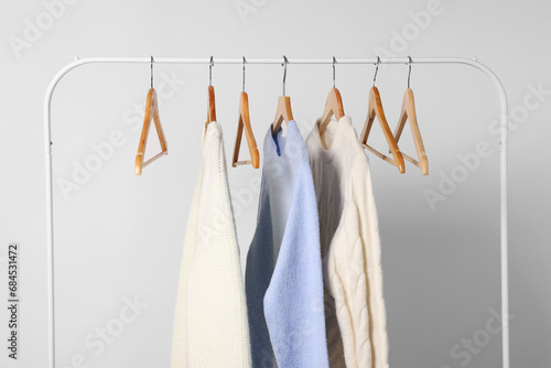 Rack with different warm sweaters on light background