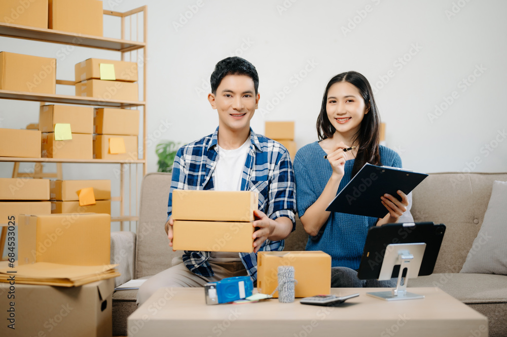 Startup small business SME, Entrepreneur owner man and woman using smartphone or tablet taking receive and checking online purchase shopping order to preparing pack product box. on sofa . Startup small business SME, Entrepreneur owner man and woman using smartphone or tablet taking receive and checking online purchase shopping order to preparing pack product box. on sofa .