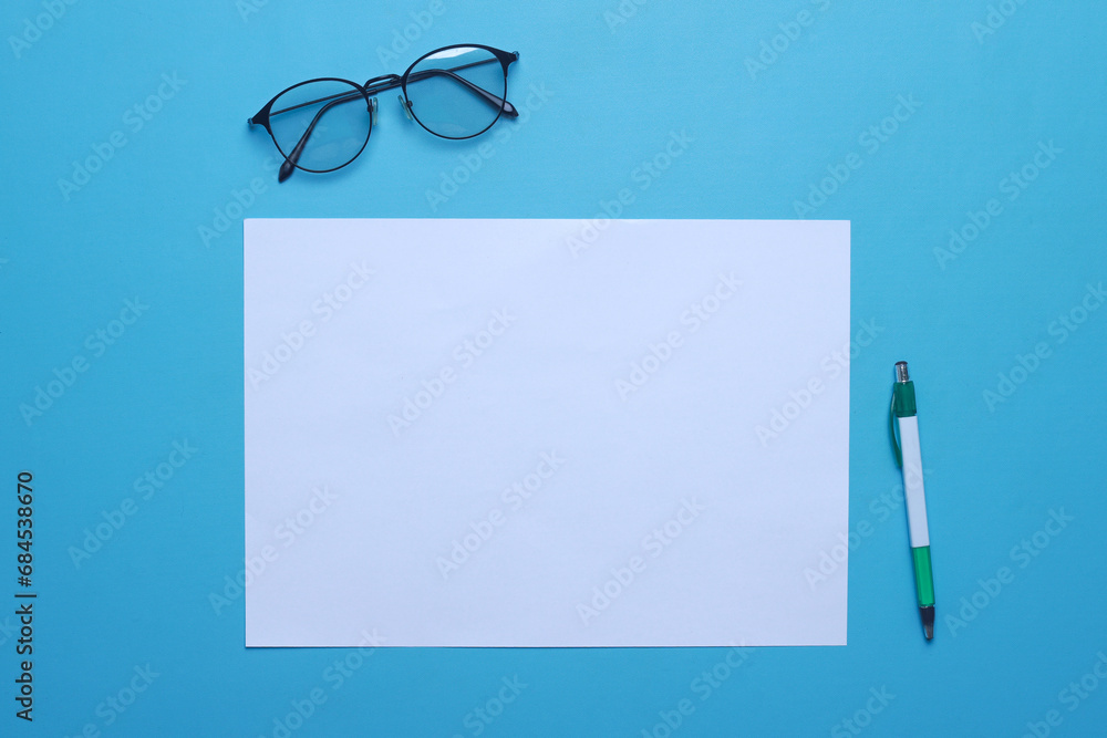 Blank horizontal paper for mock up with glasses and pen on blue background Blank horizontal paper for mock up with glasses and pen on blue background