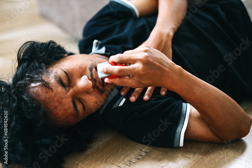 Young man with breathing difficulties using an inhaler during asthmatic attack on the floor photo