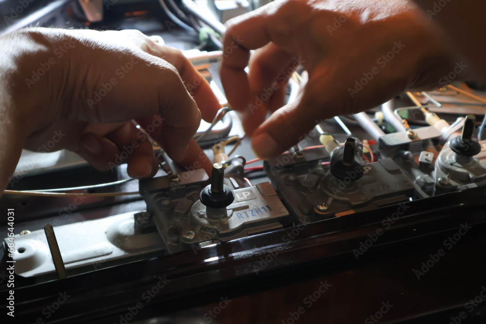 Close up of a technician's hand repairing a broken cooktop or stovetop Close up of a technician's hand repairing a broken cooktop or stovetop