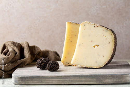 Wooden board with aged sheep's milk pecorino cheese with black truffles flakes. Fresh whole truffles on a board. Italian luxury cheese. Copy space. photo