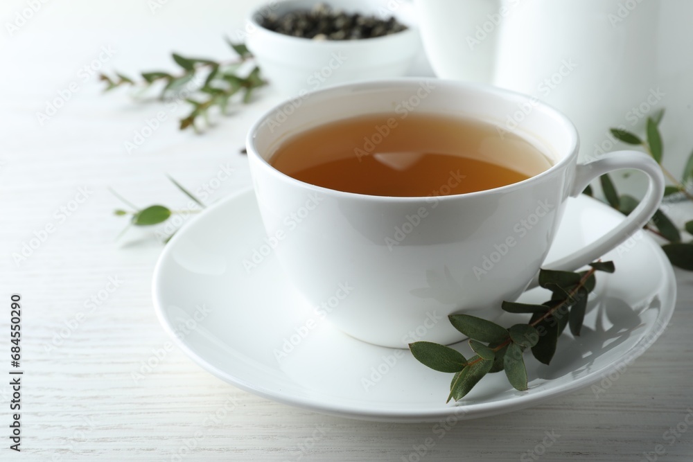 Cup of green tea and eucalyptus leaves on white wooden table Cup of green tea and eucalyptus leaves on white wooden table