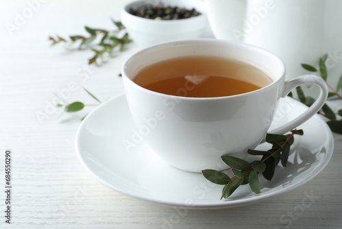 Cup of green tea and eucalyptus leaves on white wooden table