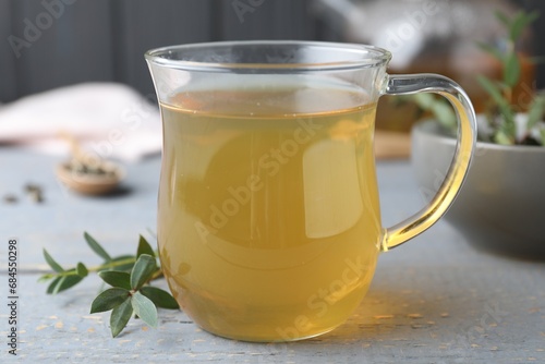 Glass cup of aromatic eucalyptus tea on grey wooden table, closeup