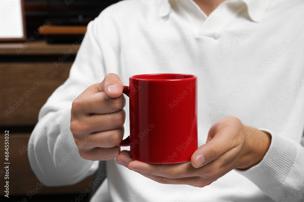 Man holding red mug indoors, closeup. Mockup for design Man holding red mug indoors, closeup. Mockup for design