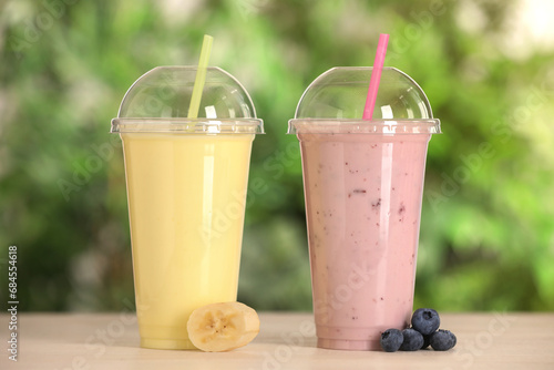 Plastic cups with different tasty smoothies and fresh fruits on wooden table outdoors