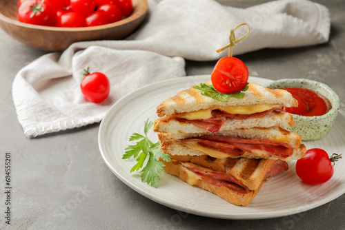 Stack of tasty sandwiches with ham and melted cheese served with tomato on grey textured table