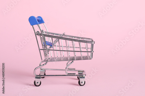 Small metal shopping cart on pink background, space for text