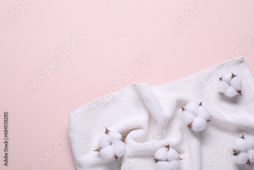 Fluffy cotton flowers and white terry towel on beige background, top view. Space for text