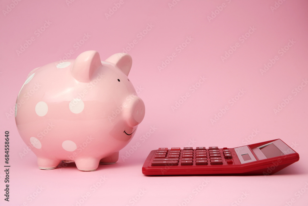 Piggy bank and calculator on pink background Piggy bank and calculator on pink background