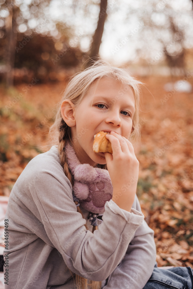A girl on a picnic in an autumn park eats a croissant. A girl on a picnic in an autumn park eats a croissant.