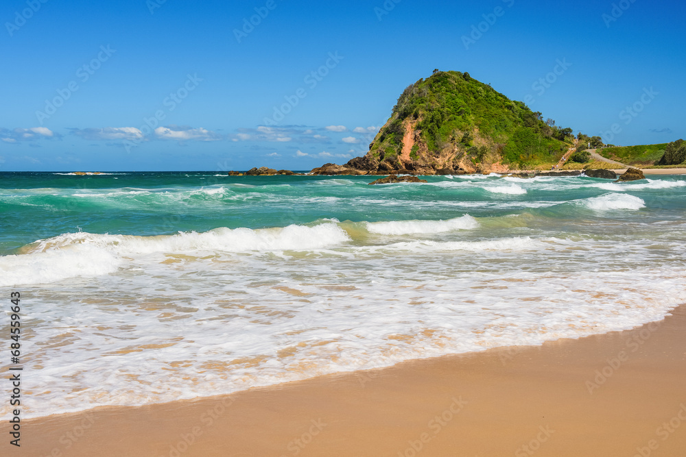 Australian coast, big rock on the seashore with blue water with waves and sandy beach, view from the beach to the seaside landscape on a summer sunny day.