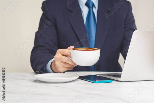 Businessman holding a cup of coffee while working at a desk.