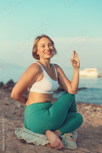 Young beautiful woman sitting in Cow Face Pose or Gomukhasana pose on the beach with hands up photo
