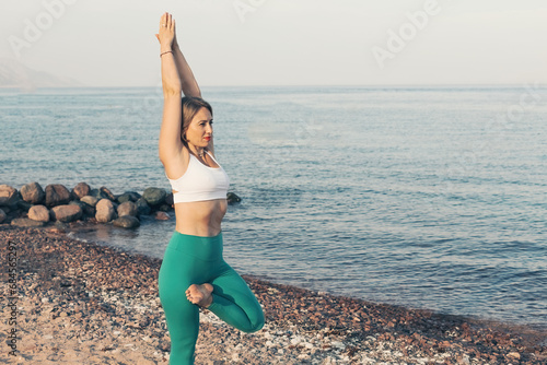 Young pretty woman performing Vriksasana tree pose yoga practice on the beach photo