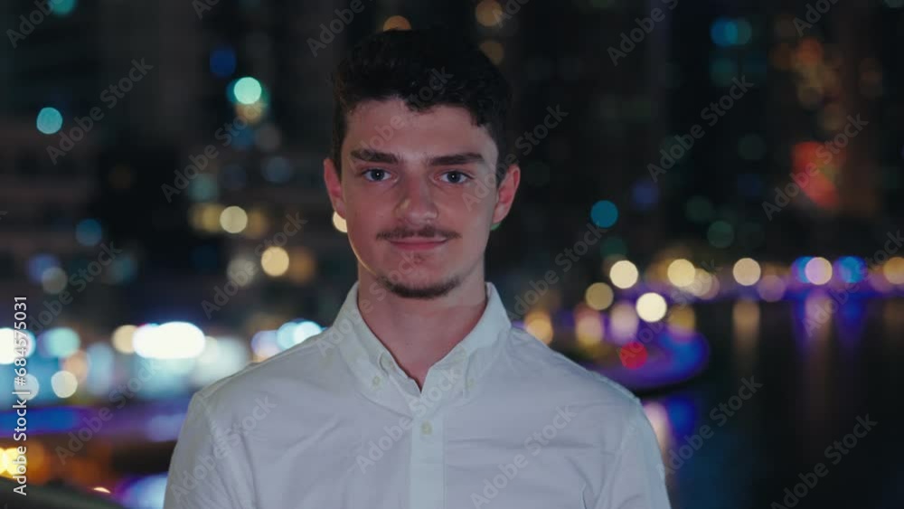 Handsome Smiling Guy Looking to the Camera, on Night Street Background. Attractive Male Wearing White Shirt Standing, Posing Outside. People Concept Handsome Smiling Guy Looking to the Camera, on Night Street Background. Attractive Male Wearing White Shirt Standing, Posing Outside. People Concept