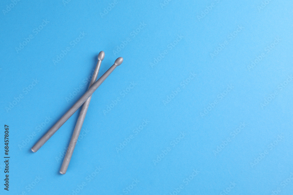 Two gray drum sticks on light blue background, top view. Space for text Two gray drum sticks on light blue background, top view. Space for text