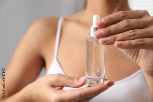 Woman with bottle of cosmetic serum on grey background  closeup