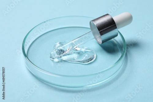 Petri dish with sample of cosmetic serum and pipette on light blue background, closeup