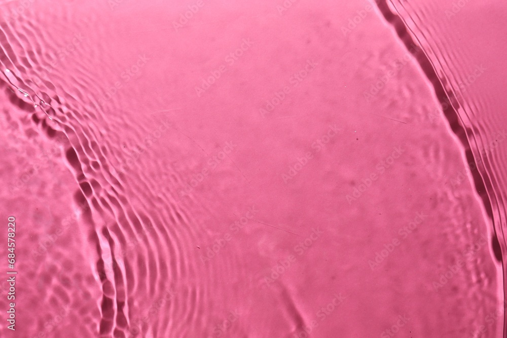 Rippled surface of clear water on bright pink background, top view Rippled surface of clear water on bright pink background, top view