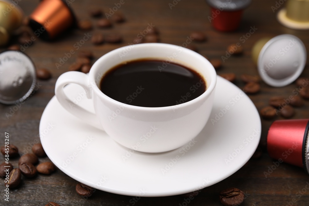 Cup of coffee, capsules and beans on wooden table, closeup