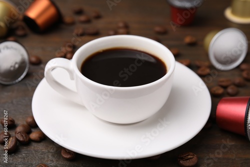 Cup of coffee, capsules and beans on wooden table, closeup