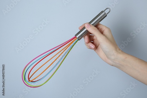 Woman holding colorful whisk on light grey background, closeup