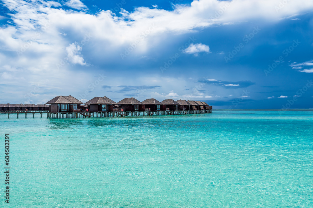 Scenic view of water villas in Maldives with turquoise water and dramatic sky