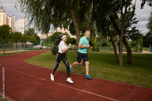 Senior couple running on track together outdoor at natural park