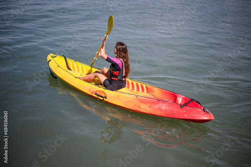 young caucasian long haired girl paddling enjoying a ride in a sit on top kayak on the mediterranean coast