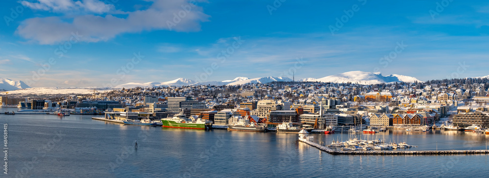 Panoramic view to Tromso harbor. White yacht sailing in the port of Tromso at sunset. Frost and first snow. Colorful winter clouds. Northern Norway