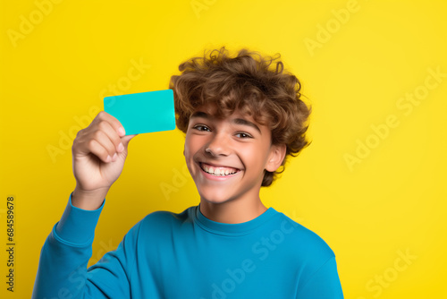 Teen age boy holds creit card on bright color background photo