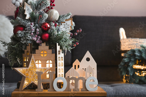 Beautiful holiday card. The concept of congratulations on the new year and Christmas 2024. Christmas wooden houses and the word home on a wooden table in a cozy living room. photo