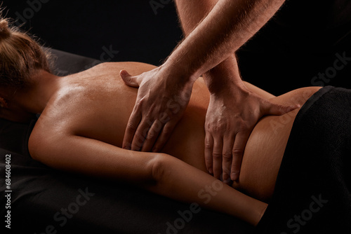 handsome male masseur giving massage to girl on black background, concept of therapeutic relaxing massage
