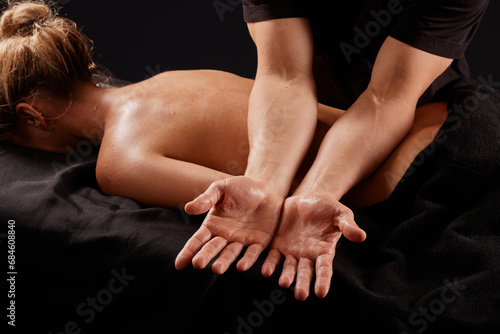 handsome male masseur giving massage to girl on black background, concept of therapeutic relaxing massage