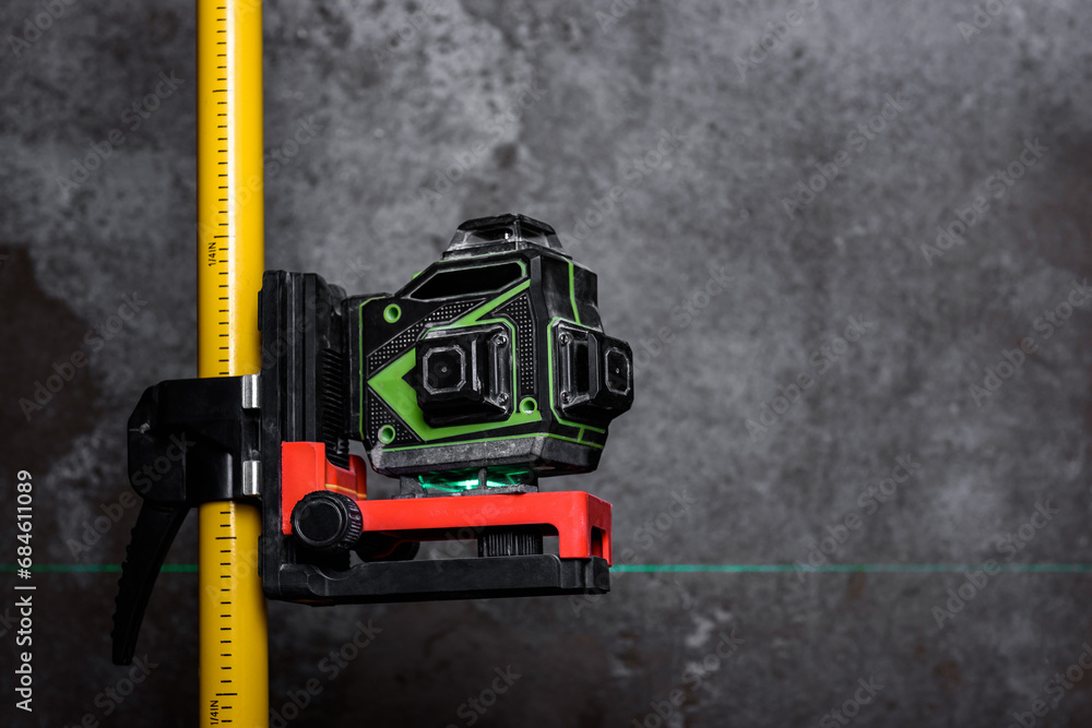 Construction laser level with green line on tripod on wall background.