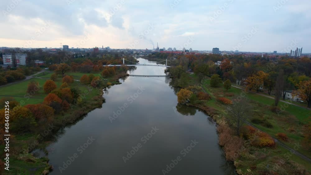 A drone captures a city park during an autumn day, flying along the river Odra and trees, revealing a vibrant carpet of yellow trees. city view A drone captures a city park during an autumn day, flying along the river Odra and trees, revealing a vibrant carpet of yellow trees. city view