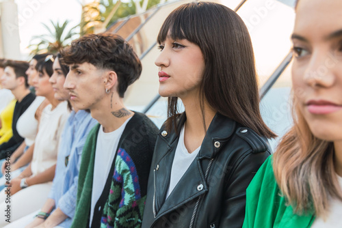 Serious young ethnic woman sitting with diverse friends in daylight on building roof