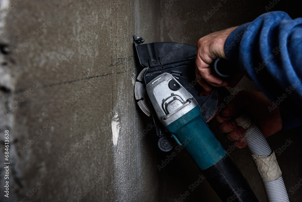 Worker holding angle grinder with two diamond discs for cutting grooves in wall. - obrazy, fototapety, plakaty 