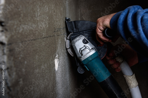 Worker holding angle grinder with two diamond discs for cutting grooves in wall. photo