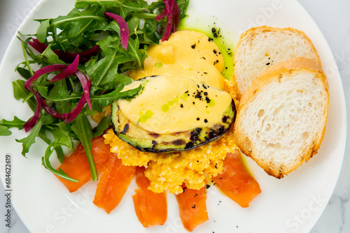 a mix of salmon, arugula salad, white bread and baked avocado with cheese top view