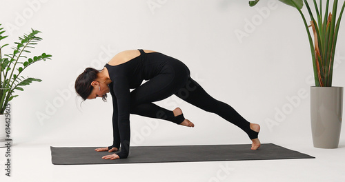 Brunette woman practicing yoga, performing Chaturanga Dandasana exercise, dynamic plank, training in a one-piece black sports overalls on a mat in the studio