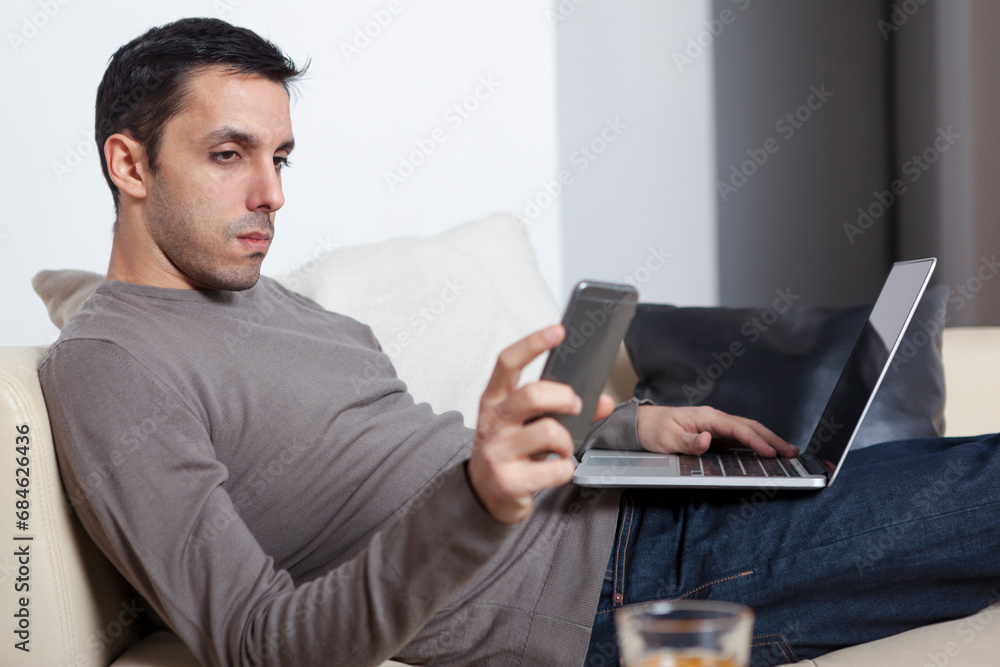 Young man working from home using laptop and smart phone Young man working from home using laptop and smart phone