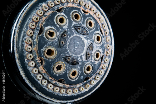 Hard water calcium or lime scale deposits on old, worn out shower head. Close up studio shot, isolated on black, no people