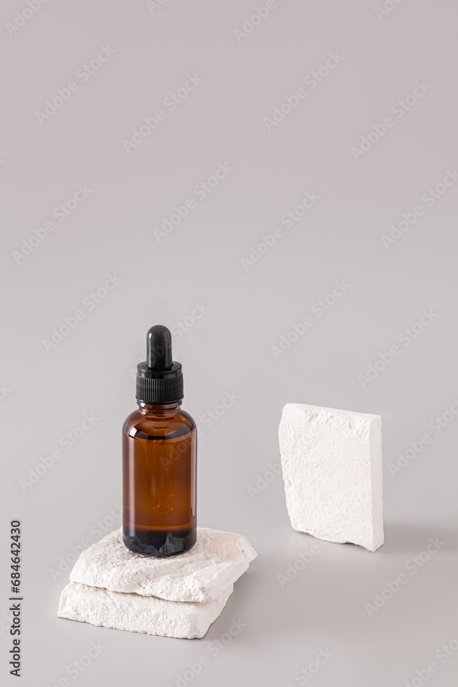 A classic cosmetic bottle with a dark glass pipette stands on two slices of white brick. Blank bottle mockup for product presentation. Vertical view.